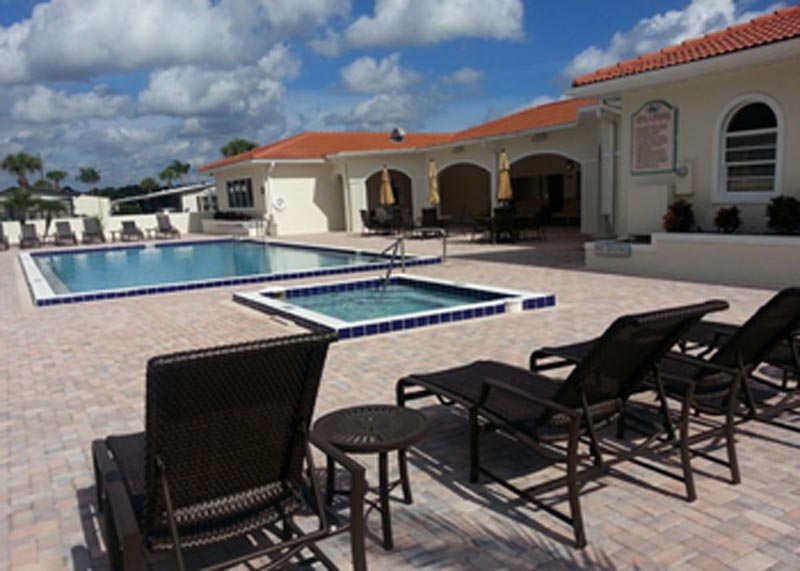 Pool and spa behind the clubhouse surrounded by brick patio and lounge chairs.