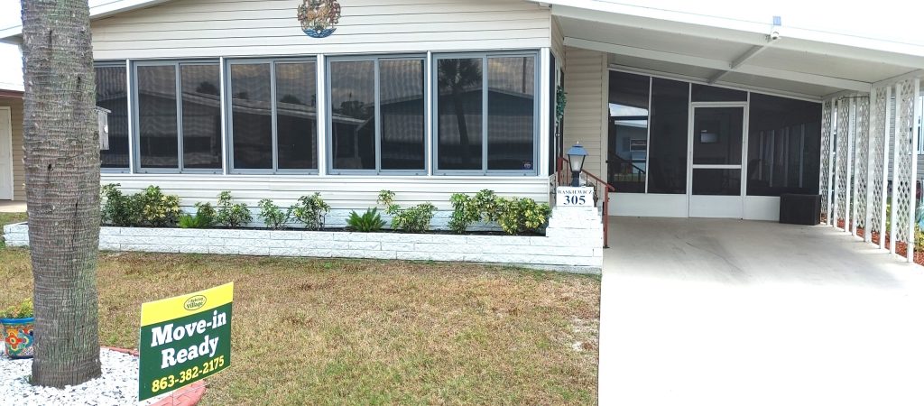 Single-story house with large front windows, a covered driveway, and a "Move-in Ready" sign on the lawn with a phone number.